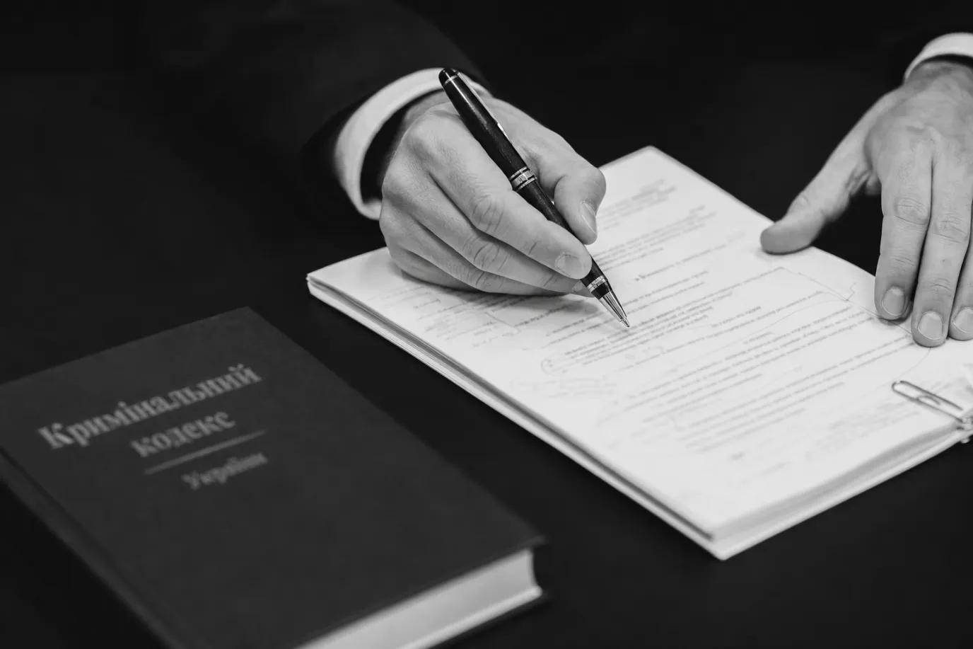 Руки адвоката з ручкою над матеріалами справи про хуліганство ст. 296 КК